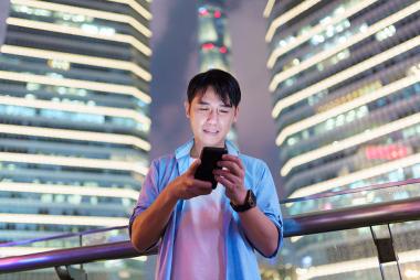 男人看着他的手机屏幕，站在三栋灯火通明的高楼前