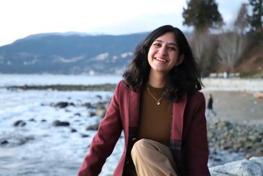 开云体育最新网站UBC材料工程专业的学生Gauri Taneja坐在海滩上，对着镜头微笑，远处是海洋和山脉。